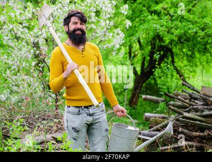 Bewässerung. Gartenarbeit. Lächelnder Gärtner mit Gießkanne und Spaten. Arbeiten im Garten. Bauernhof. Frühling Stockfoto