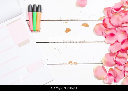 Foto von farbigen Leuchtstofflampen und einem Notizblock auf einem Holzhintergrund weiß und geschmückt mit Rosenblättern.das Foto ist Eine Aufnahme über dem Kopf mit Horizont Stockfoto