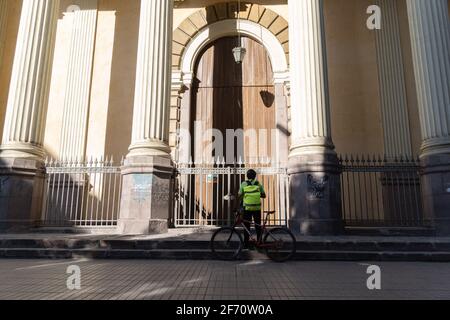 Santiago, Metropolitana, Chile. April 2021. Ein Radfahrer hält an, um am Karsamstag vor einer Kirche zu beten, die wegen totaler Quarantäne in Santiago geschlossen wurde. Quelle: Matias Basualdo/ZUMA Wire/Alamy Live News Stockfoto