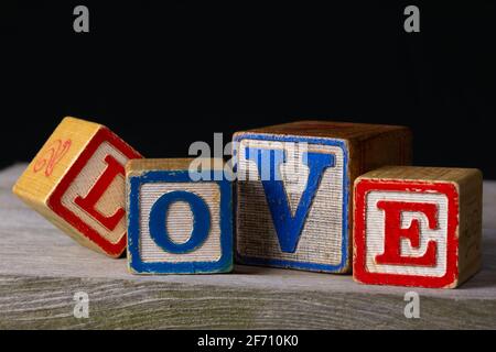 „Love“, geschrieben in alten Holzblöcken auf altem Holz und schwarzem Hintergrund. Stockfoto