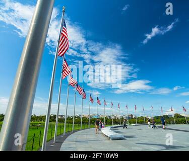 An einem sonnigen Tag weht eine Reihe amerikanischer Flaggen auf Fahnenmasten im Wind um das Washington Monument in Washington, D.C. Stockfoto