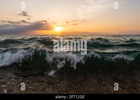 Eine Welle stürzt in die Meeresküste als die Sonne Setzt sich in den bunten Sonnenuntergang Himmel Stockfoto