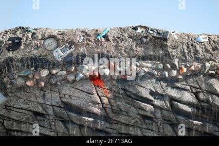 Alttechnologiemüll teilweise im Boden eingebettet. Alte Telefone, Computerteile und Tonbandgeräte in Sedimentation und Gesteinsschichten. Stockfoto
