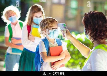 Temperaturkontrolle und ärztliche Untersuchung in der Schule. Kind in Gesichtsmaske in der Klasse bei Covid-19-Ausbruch. Lehrer mit Thermometer am Eingang der Vorschule. Stockfoto