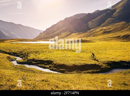 Mann auf Mountainbike-Fahrten in der Nähe des Sees im grünen Bergtal bei Sonnenaufgang. Freizeit, Reisen und gesundes Lifestyle-Konzept. Stockfoto