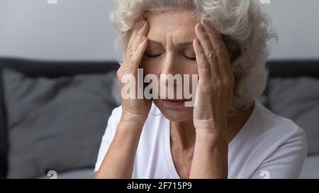 Gestresste frustrierte ältere Frau mit starken schmerzhaften Kopfschmerzen Stockfoto