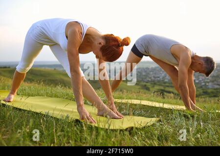 Fit Mann und Frau in Fitness-Kleidung dabei Parsvottanasana Gemeinsam Yoga in der Natur im Sommer praktizieren Stockfoto