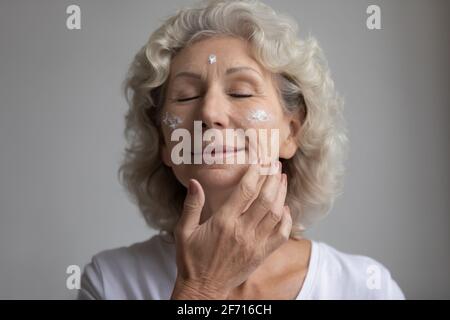 Entspannte ältere Frau mit geschlossenen Augen, die eine Hautpflege einnahm Stockfoto