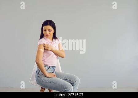 Glückliche junge Dame, die auf einem Stuhl sitzt, zeigt ihren Arm Nach dem Erhalt eines Covid-19 Schusses Stockfoto