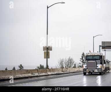 Schwarz Big Rig industriellen Auto Schlepper Semi-Truck mit leer Doppeldeck hydraulische modulare Sattelauflieger laufen auf dem rutschigen Nasse Straße mit Spiegelung Stockfoto