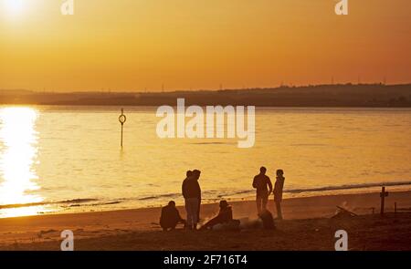 Portobello, Edinburgh, Schottland, UK Wetter. April 2021. Atemberaubender Sonnenaufgang am Ostersonntag am Meer, Temperatur 5 Grad Celsius. Menschen mit einem Lagerfeuer am Strand und einem Kreuz im Sand rechts von Bildern. Stockfoto