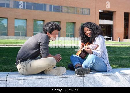 Ein junger lateinmann lehrt einer jungen lateinerin auf dem Universitätscampus, wie man Gitarre spielt. Universitätsleben, tausendjährige Generation. Stockfoto