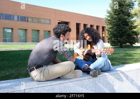 Ein junger lateinmann lehrt einer jungen lateinerin auf dem Universitätscampus, wie man Gitarre spielt. Universitätsleben, tausendjährige Generation. Stockfoto