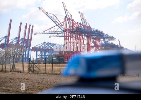 Hamburg, Deutschland. März 2021. Das blaue Licht eines Patrouillenwagens vor Containerbrücken an einem Containerterminal. Die Hamburger Polizei setzte ein großes Kontingent ein, um nach einem möglicherweise verletzten Fahrer zu suchen, der aus einer Verkehrskontrolle geflohen war und daraufhin einen Unfall verursacht hatte. Quelle: Jonas Walzberg/dpa/Alamy Live News Stockfoto