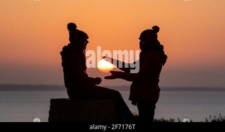 Bournemouth, Großbritannien. April 2021. Ein Paar genießt den Moment, in dem die Sonne am Ostertag am Hengistbury Head in Bournemouth, Dorset, aufgeht, am Beginn eines hellen und sonnigen Tages an der Südküste. Kredit: Richard Crease/Alamy Live Nachrichten Stockfoto