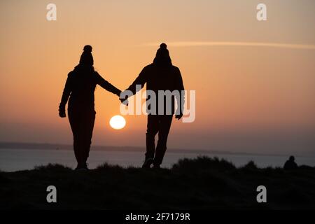 Bournemouth, Großbritannien. April 2021. Ein Paar genießt den Moment, in dem die Sonne am Ostertag am Hengistbury Head in Bournemouth, Dorset, aufgeht, am Beginn eines hellen und sonnigen Tages an der Südküste. Kredit: Richard Crease/Alamy Live Nachrichten Stockfoto