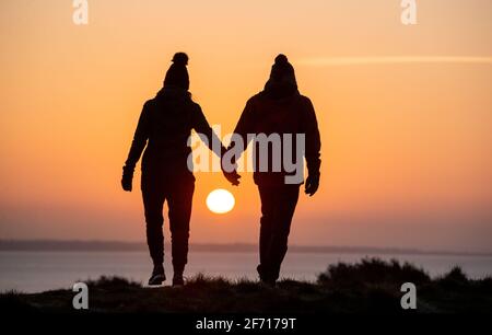 Bournemouth, Großbritannien. April 2021. Ein Paar genießt den Moment, in dem die Sonne am Ostertag am Hengistbury Head in Bournemouth, Dorset, aufgeht, am Beginn eines hellen und sonnigen Tages an der Südküste. Kredit: Richard Crease/Alamy Live Nachrichten Stockfoto