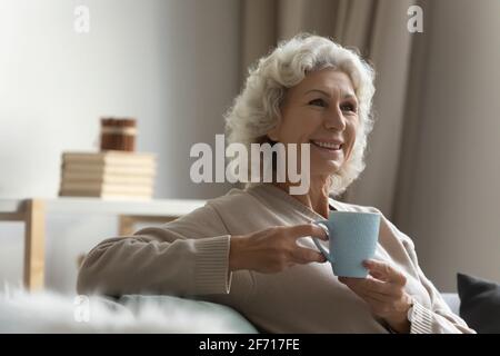 Glückliche ältere Dame, die zu Hause eine Tasse heißes Getränk genießt Stockfoto