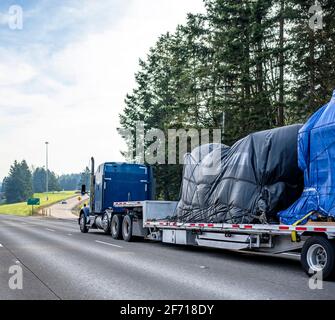 Riesige blaue klassische große Rig Industrie-Semi-Truck Transport abgedeckt Mit Plane schwere kommerzielle Ladung auf Schritt-down-Sattelauflieger Laufen auf der breiten Hi Stockfoto