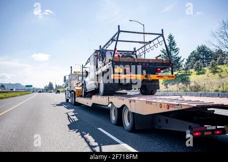 Riesige weiße klassische große Rig Industrie-Semi-Truck Transport ein anderes Stapler mit Rahmen auf heruntergefahrendem Sattelauflieger Die breite gerade Autobahn Stockfoto