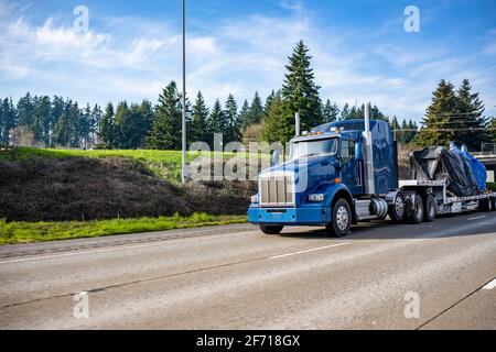 Riesige blaue klassische große Rig Industrie-Semi-Truck Transport abgedeckt Mit Plane schwere kommerzielle Ladung auf Schritt-down-Sattelauflieger Laufen auf der breiten Hi Stockfoto