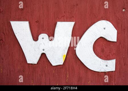 Weiße WC-Buchstaben auf rot ockerfarbener Sperrholztür Stockfoto