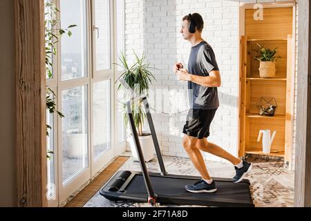 Der junge Mann joggt auf dem modernen kompakten Laufband bei ihm Zu Hause Stockfoto
