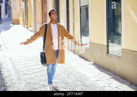 Ein junger schwarzer Mann, der die Straße entlang läuft, trägt eine Aktentasche und ein Smartphone. Stockfoto