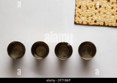 Matzah - Jüdisches Brot zum Passah. Neben vier silbernen Tassen. Weißer Hintergrund Stockfoto