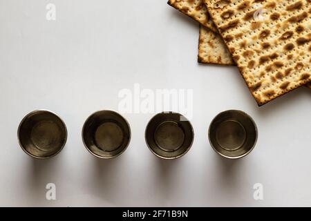 Drei Matzahs - Jüdisches Brot für Passah. Neben vier silbernen Tassen. Weißer Hintergrund Stockfoto