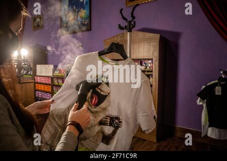 Moskau, Russland. April 2021. Ein Mitarbeiter des Geschäfts dampft T-Shirts in einem Souvenirshop mit abbildbaren Figuren des computeranimierten Comedy-Films Hotel Transylvania im Vergnügungspark Dream Island in Moskau, Russland Stockfoto