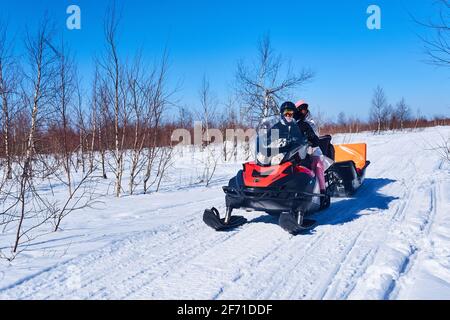 Russland, Region Perm - 28. März 2021: Die Menschen fahren auf einer Winterstraße zwischen einer Birkenwald-Tundra mit einem Schneemobil Stockfoto