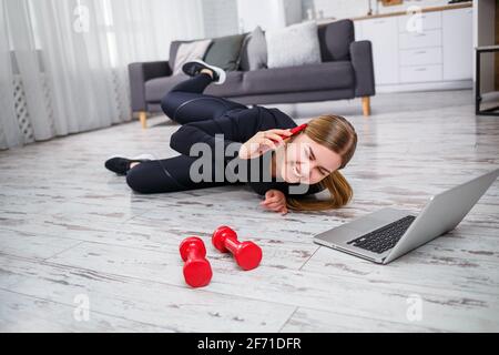 Schöne athletische Frau in einem schwarzen Oberteil und Leggings, die zu Hause Sport treiben und telefonieren. Motivation zum Sport. Gesunder Lebensstil. Stockfoto