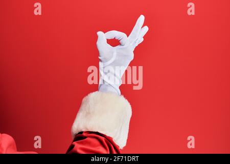 Hand eines Mannes mit weihnachtsmann Kostüm und Handschuhen Auf rotem Hintergrund gestikulierte Genehmigung Ausdruck tut okay Symbol mit Finger Stockfoto