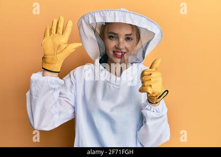 Schöne blonde kaukasische Frau trägt schützende Imker Uniform zeigen und Zeigt mit den sechs Fingern nach oben und lächelt zuversichtlich und happ Stockfoto