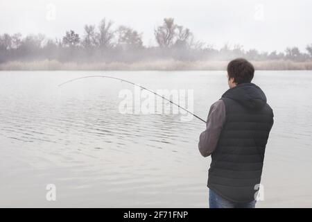 Fisher man fischt mit Spinnrute an einem Flussufer bei neblig nebligen Sonnenaufgang. Stockfoto