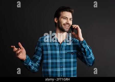 Fröhlich hübsch Brünette Kerl lächeln und sprechen auf Handy isoliert Auf schwarzem Hintergrund Stockfoto