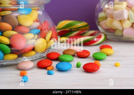 Mehrfarbige Bonbons in Gläsern auf einem weißen Tisch. Nahaufnahme. Lila Hintergrund Stockfoto