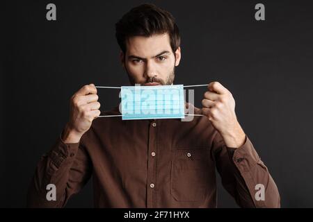 Ernst schöner junger Mann posiert mit Schutzmaske isoliert über Schwarzer Hintergrund Stockfoto