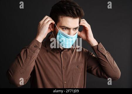 Fokussierter, hübscher junger Mann, der in einer Schutzmaske posiert und isoliert darüber liegt Schwarzer Hintergrund Stockfoto