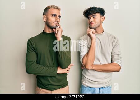 Homosexuell Gay Paar stehend zusammen tragen lässige Kleidung Denken konzentriert Über Zweifel mit Finger auf Kinn und Blick nach oben fragen Stockfoto