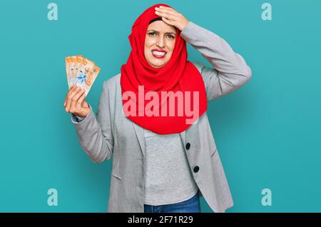 Schöne hispanische Frau mit islamischem Hijab, die 10 schweizer Franken-Banknoten hält, gestresst und frustriert, mit der Hand am Kopf, überrascht und wütend Stockfoto