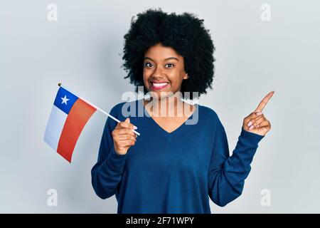 Junge afroamerikanische Frau, die die chilenische Flagge hält, lächelt glücklich und zeigt Mit Hand und Finger zur Seite Stockfoto