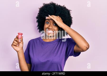 Junge afroamerikanische Frau mit Menstruationsbecher gestresst und frustriert mit Hand auf dem Kopf, überrascht und wütend Gesicht Stockfoto