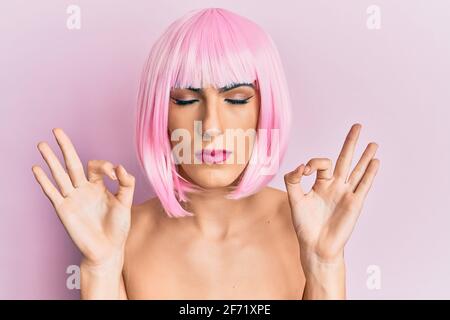 Junger Mann trägt Frau Make-up trägt rosa Perücke entspannen und lächeln mit geschlossenen Augen tun Meditation Geste mit den Fingern. Yoga-Konzept. Stockfoto