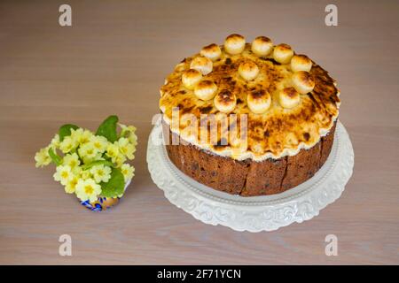 Ostergenuss: Ein ungeschnittener traditioneller, hausgemackter runder Simnellkuchen - Obstkuchen mit geröstetem Marzipan-Belag, verziert mit runden Marzipankugeln Stockfoto