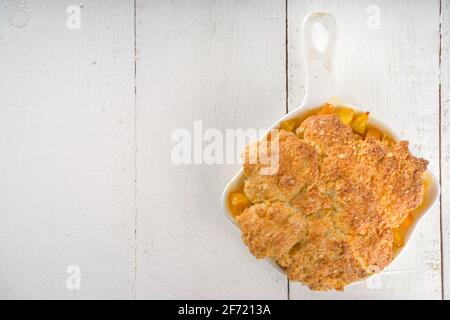 Köstlicher Summer Peach Cobbler, hausgemachter süßer Sommerkuchen mit Pfirsichen und Vanilleeis auf weißem Holzhintergrund Stockfoto