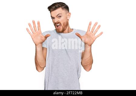 Junger rothaariger Mann trägt lässiges graues T-Shirt Angst und erschrocken vor Angst Ausdruck Stop-Geste mit Händen, schreiend in Schock. Panikkonzept. Stockfoto