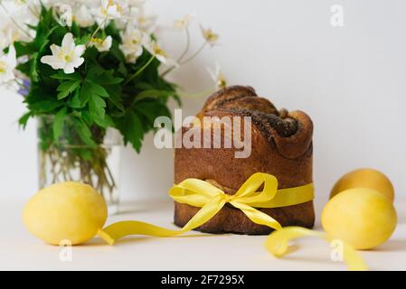 Osterkuchen, gelb bemalte Eier und Blumen auf einem beigen Tisch. Frühlingsfeiertage. Traditionelle Festtafel. Speicherplatz kopieren Stockfoto