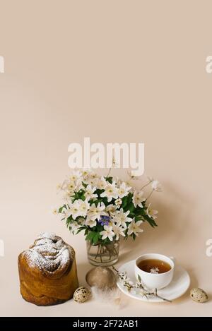 Osterkarte. Ein Kuchen, eine Tasse Tee, Primeln in einer Vase und Wachteleier auf beigem Hintergrund. Platz kopieren Stockfoto